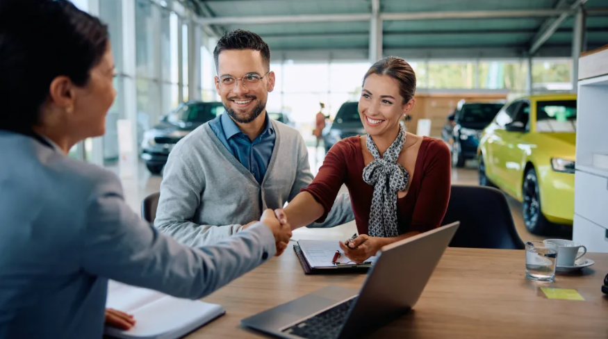 Couple shaking hands with saleswoman after buying a new car.