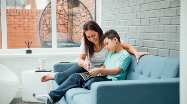 Mother and son reading a book together in the living room.